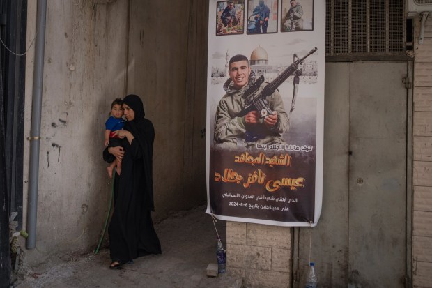 A woman carrying her child passes a banner with a picture of Issa Jallad, 17, who was killed by Israeli forces during a raid two days earlier in Jenin, West Bank, Saturday, June 8, 2024. (AP Photo/Bram Janssen)