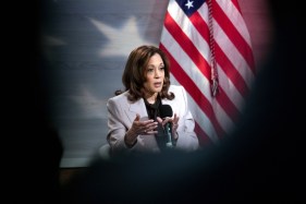 Vice President Kamala Harris speaks into a microphone in front of an American flag