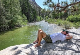 A man lies on his back on a boulder along a river